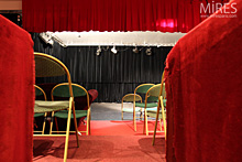 Petite salle avec une scène, rideaux rouges, chaises vertes. C0685