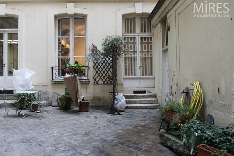 C0686 – Cour pavée avec table, fontaine et plantes en pots